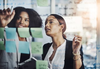 Two female executive assistants building a meeting agenda on a board