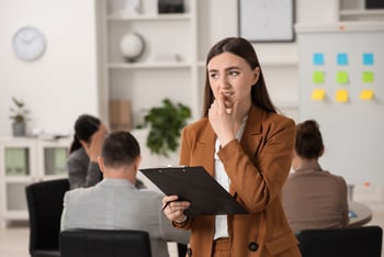 Nervous looking Executive Assistant biting her finger in a meeting while holding a clipboard