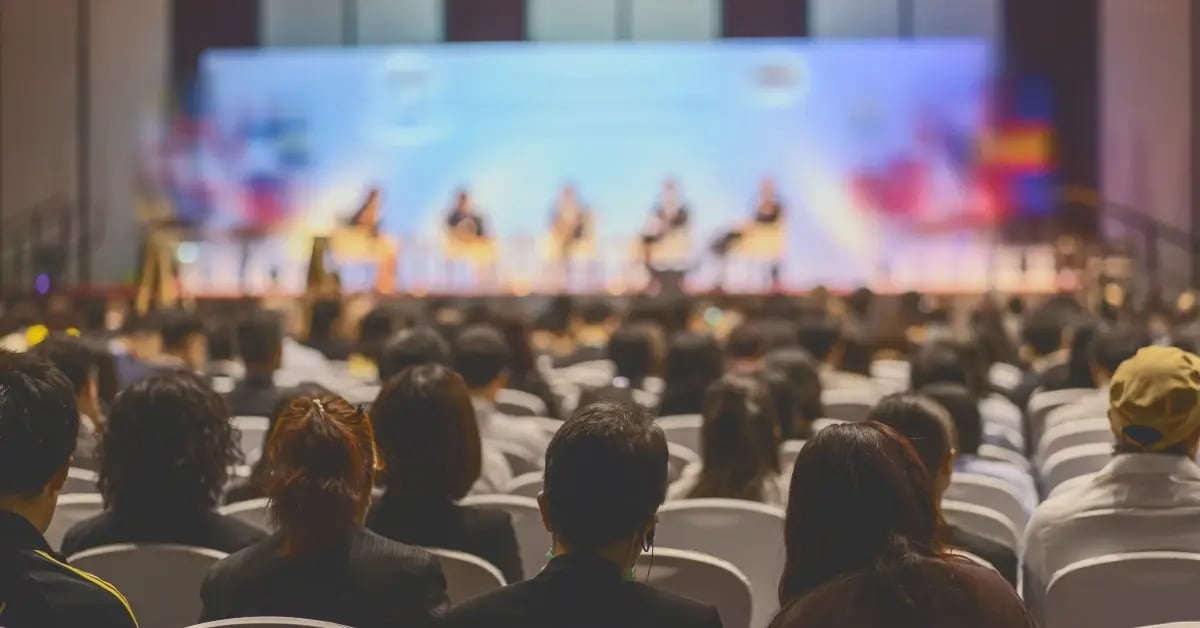 Audience sitting in seats at an event looking at the stage of speakers