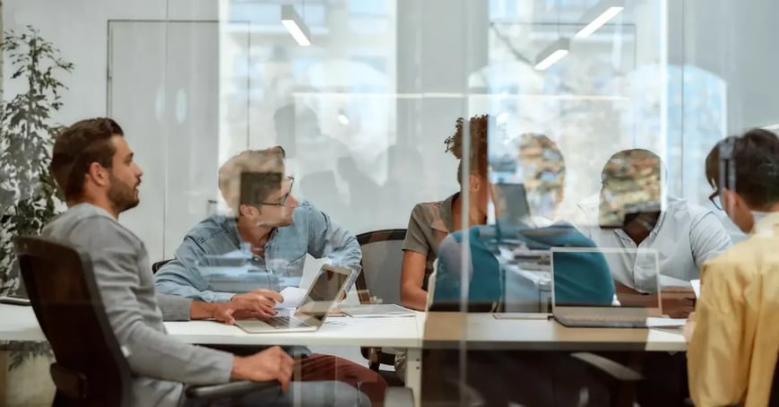 Behind a conference room window is a team of meeting planners talking about their upcoming offsite