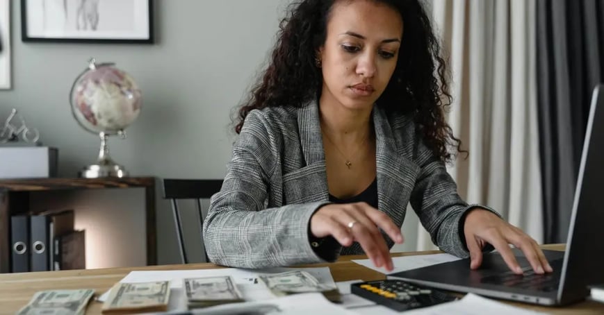 EA calculating her in-person meeting budget at her desk on her calculator and computer