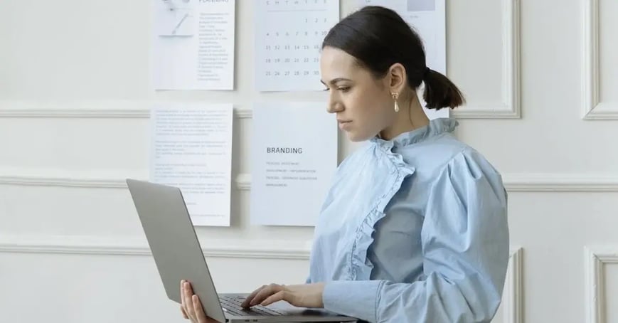 Executive Assistant standing and looking at her computer as she plans simple meetings