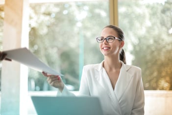 Executive Assistant sitting behind her computer, handing off a offsite location plan to her boss