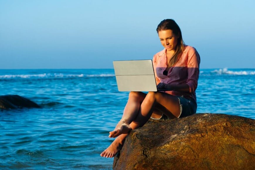 A woman sitting at the beach working remotely