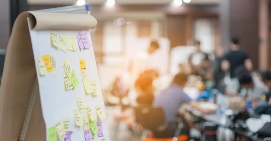 Post it notes on a board with a blurred group of attendees in the background