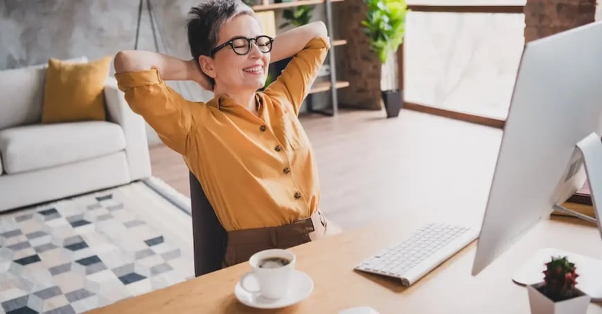 Satisfied Executive Assistant leaning back in her chair, with her arms crossed behind her head, looking at her computer