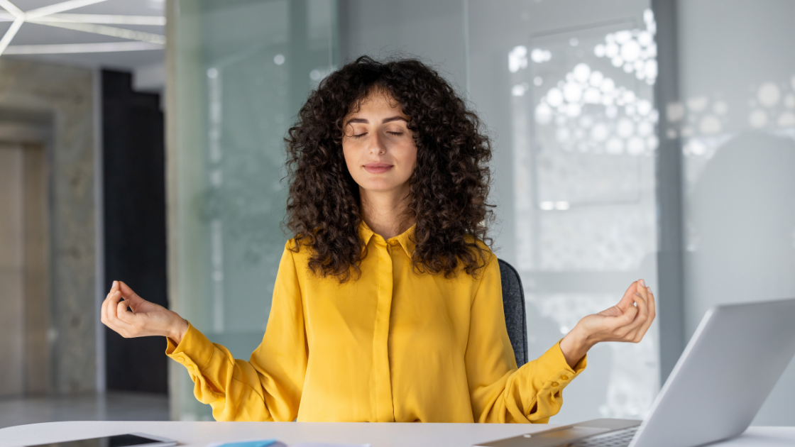 Executive Assis meditating at office desk with closed eyes. Practicing mindfulness and relaxation for stress relief during work